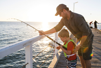 father teaching little young son to be a fisherman, fishing together on sea dock embankment enjoying and learning using the fish rod