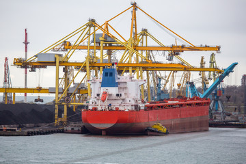 Naklejka premium Seaport coal terminal with ships standing under unloading. coal terminal of seaport. Heaps of coal in port awaiting loading on ship and shipment all over world