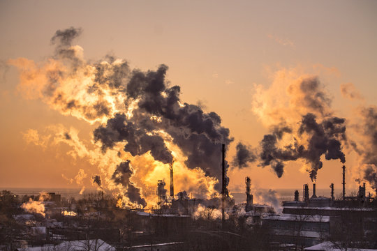 the chimneys of a refinery with smoke and steam with the pinkk sunset on the background