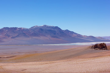 Intense pastel colored landscape of Atacama Desert landscape after sunrise, Chile. High altitude desert and volcanic mountains colored by rising sun in light lilac hue on horizon.