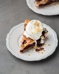 A piece of cherry pie with vanilla ice cream on a white vintage plate on a gray light concrete background. Copy Space. View blank space for text.