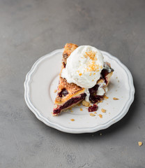 A piece of cherry pie with vanilla ice cream on a white vintage plate on a gray light concrete background. Copy Space. View blank space for text.