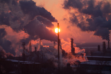 the chimneys of a refinery with smoke and steam with the pinkk sunset on the background