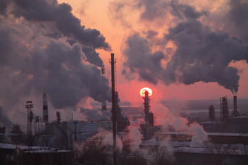 the chimneys of a refinery with smoke and steam with the pinkk sunset on the background