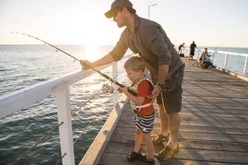 Stof per meter vader die kleine jonge zoon leert visser te worden, samen vissen op de dijk van de zeedok, genietend en lerend met de vishengel © Wordley Calvo Stock