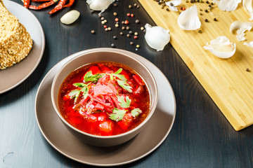 Red borscht soup with parsley in brown bowl top view, on black table.
