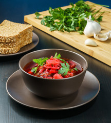 Red borscht soup with parsley in brown bowl top view, on black table.