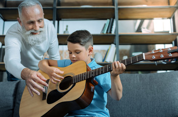 Talented generation. Selective focus on a smart little boy holding a guitar and listening to his grandfather attentively while learning how to play guitar.
