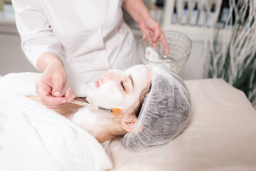 Obraz na płótnie Canvas Young pretty woman receiving treatments in beauty salons. Young beautiful dark-haired woman in the office beautician lying on the couch. Facial cleansing foam using.