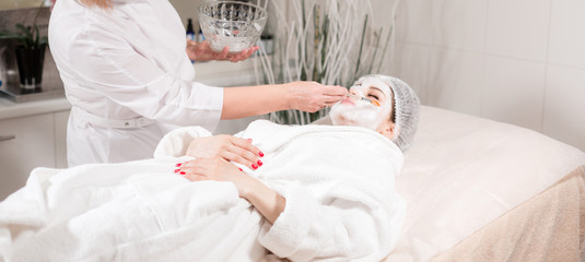 Young pretty woman receiving treatments in beauty salons. Young beautiful dark-haired woman in the office beautician lying on the couch. Facial cleansing foam using.