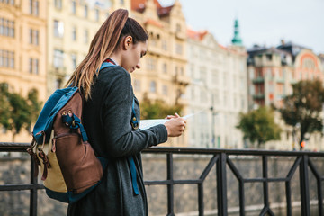 A tourist with a backpack in front of a beautiful old architecture in Prague in the Czech Republic. She looks at the map.