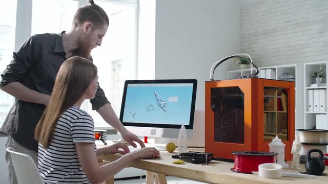 Young male designer explaining female colleague how to create 3D model for printing with computer software