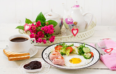 Breakfast on Valentine's Day - fried egg in the shape of a heart, toasts, sausage and fresh vegetables. Cup of coffee. English breakfast