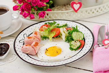 Breakfast on Valentine's Day - fried egg in the shape of a heart, toasts, sausage and fresh vegetables. Cup of coffee. English breakfast