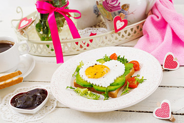 Breakfast on Valentine's Day - sandwich of fried egg in the shape of a heart, avocado and fresh vegetables. Cup of coffee. English breakfast.