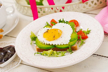 Breakfast on Valentine's Day - sandwich of fried egg in the shape of a heart, avocado and fresh vegetables. Cup of coffee. English breakfast.