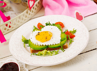 Breakfast on Valentine's Day - sandwich of fried egg in the shape of a heart, avocado and fresh vegetables. Cup of coffee. English breakfast.