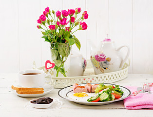 Breakfast on Valentine's Day - fried egg in the shape of a heart, toasts, sausage and fresh vegetables. Cup of coffee. English breakfast