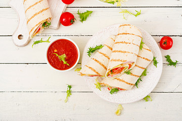 Tortilla wrap with ham, cheese and tomatoes on a white wooden background. Top view