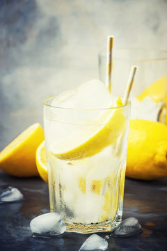 Summer refreshing drink, cold sparkling water with ice and lemon, gray background, selective focus