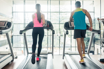 Full length rear view of a fit woman and her cardio workout, partner running on treadmills side by...