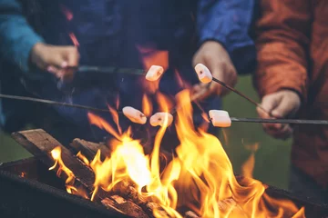 Keuken foto achterwand Kamperen Handen van vrienden die marshmallows roosteren boven het vuur in een grillclose-up