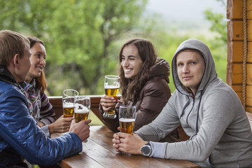 Happy friends sitting with tall glasses of beer in hand at a wooden table