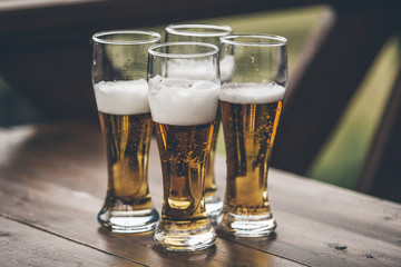 Beer with foam light tall boys standing on a wooden table closeup