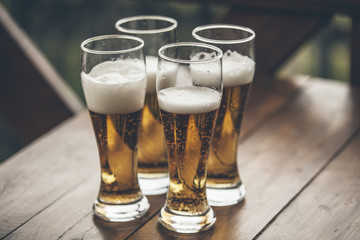 Beer with foam light tall boys standing on a wooden table closeup