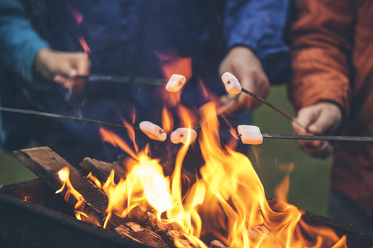Hands of friends roasting marshmallows over the fire in a grill closeup