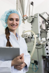 Portrait of a quality control female inspector smiling and looking at camera while holding a tablet during inspection in a contemporary cosmetics factory