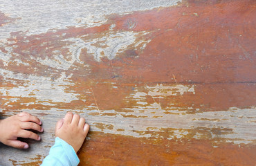 Child's hands located on brown old wooden boards background