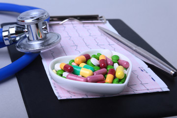 Stethoscope, RX prescription and colorful assortment pills and capsules on plate.
