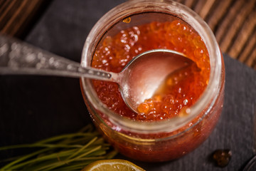 close up of salmon roe red caviar fish egg in a glass jar with spoon 