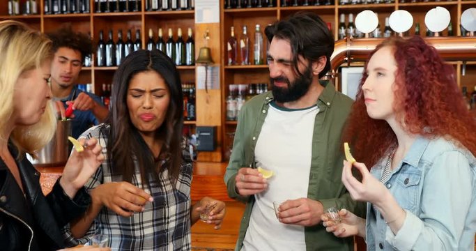 Friends having tequila shot at counter in bar 