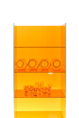 Set of various colored glass bottles, wine-glasses, goblets on yellow showcase. white background.