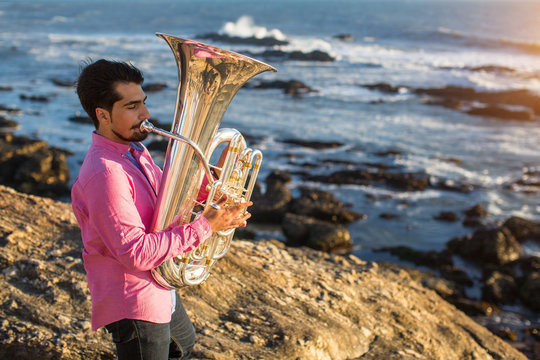 Young man play the trumpet on rocky sea coast during surf.