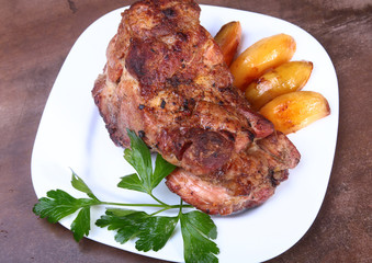 Juicy pork neck chops are grilled with potatoes on a white plate.
