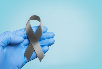 The doctor's hands in gloves hold a gray ribbon, Brain cancer awareness, Brain Tumors, Asthma awareness, Allergies and Diabetes awareness
