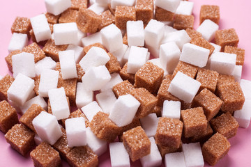 White and brown cane sugar cubes scattered on a pink background. Texture background