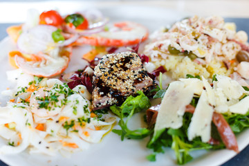 Mediterranean cuisine closeup. Mix of sea food. Grilled tuna, different seafood, vegetables and parmesan cheese.