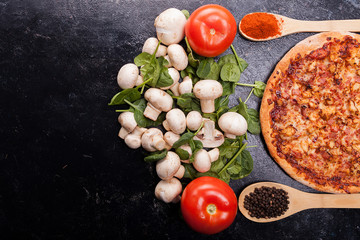 Top view on pizza, tomatoes, mushrooms and spinach on dark wooden table with copy space availabe
