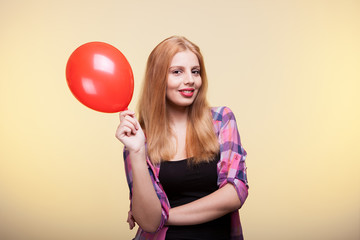 Woman holding a balloon in hands and looking at the camera on yellow background