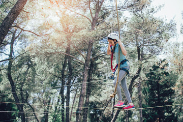 Fototapeta na wymiar Happy school girl enjoying activity in a climbing adventure park on a sunny day