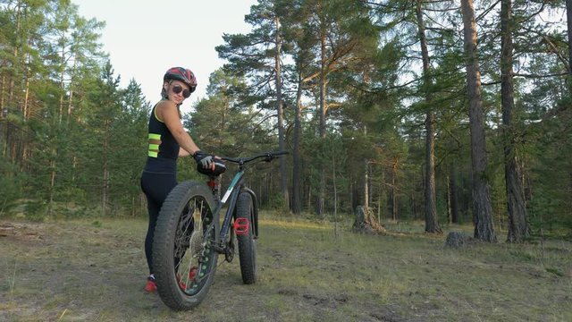 Fat bike also called fatbike or fat-tire bike in summer riding in the forest. Beautiful girl and her bicycle in the forest. She is posing near the bicycle.