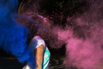 Brunette young woman with hair in motion having fun with colorful Holi powder