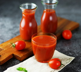 natural and healthy tomato juice in glass jars and a glass on a grey stone background. 