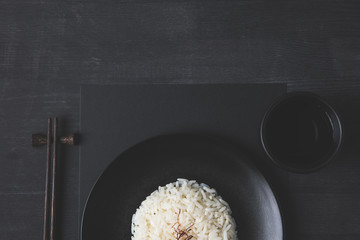top view of rice on plate with cup of tea and chopsticks on black table