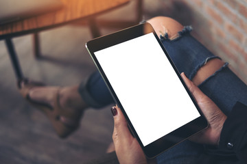 Mockup top view image of a woman wearing ripped jean sitting cross legged , holding black tablet pc with blank white desktop screen on thigh in cafe