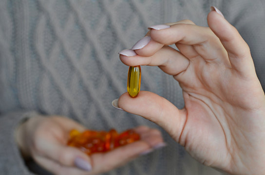 Woman's hands holding omega 3 fish oil capsula over knitted sweater background